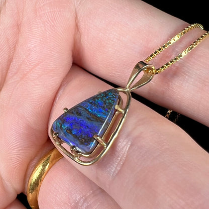 A dainty Duck Creek opalized wood necklace in 9k gold, shown close-up in a hand from an angle.