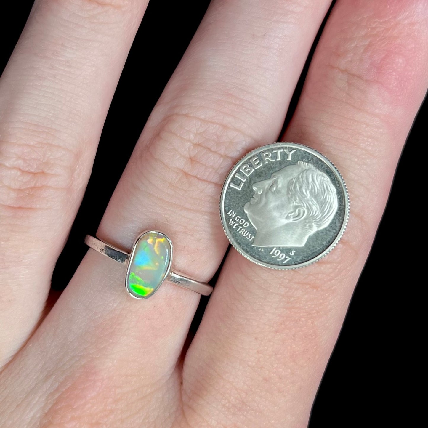 A dainty, handmade crystal opal ring in sterling silver, worn on a hand next to a US dime coin for scale.
