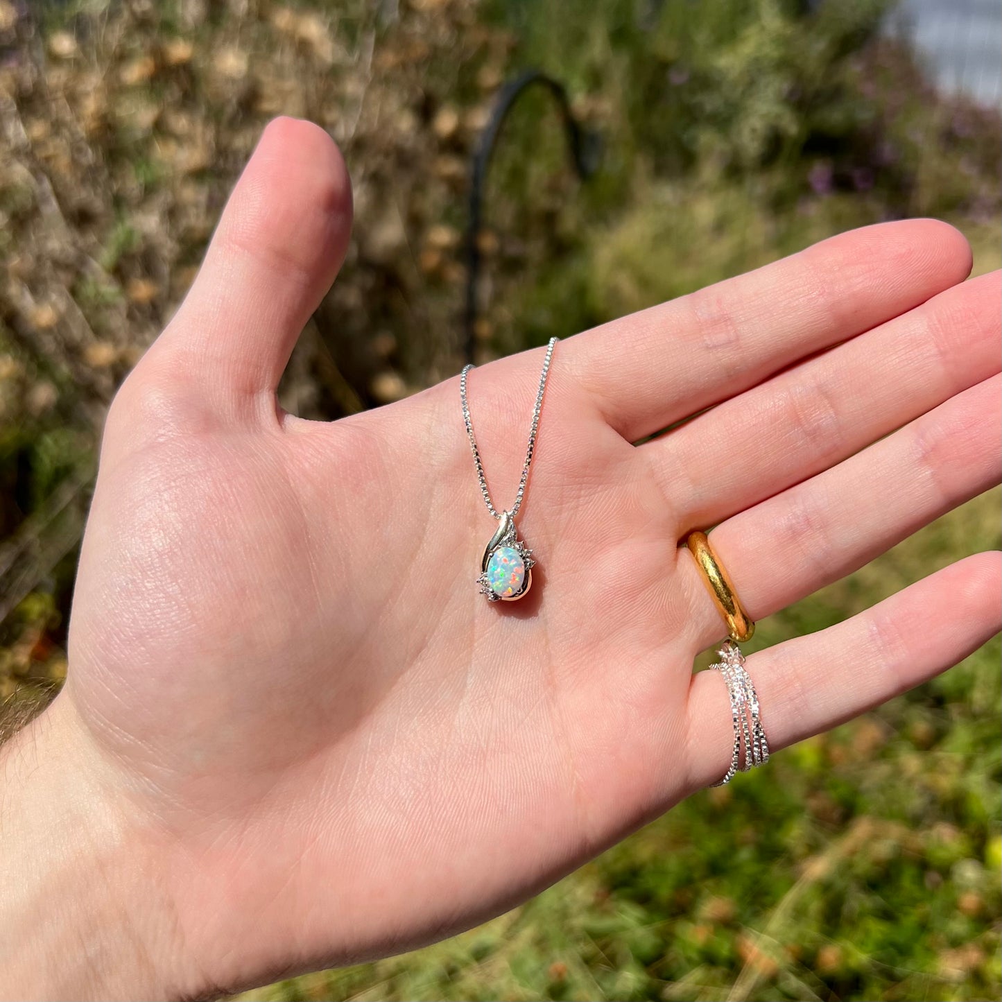 A dainty lab-created opal and diamond-accented necklace in two-tone sterling silver and 10k gold, held in a hand in sunlight.