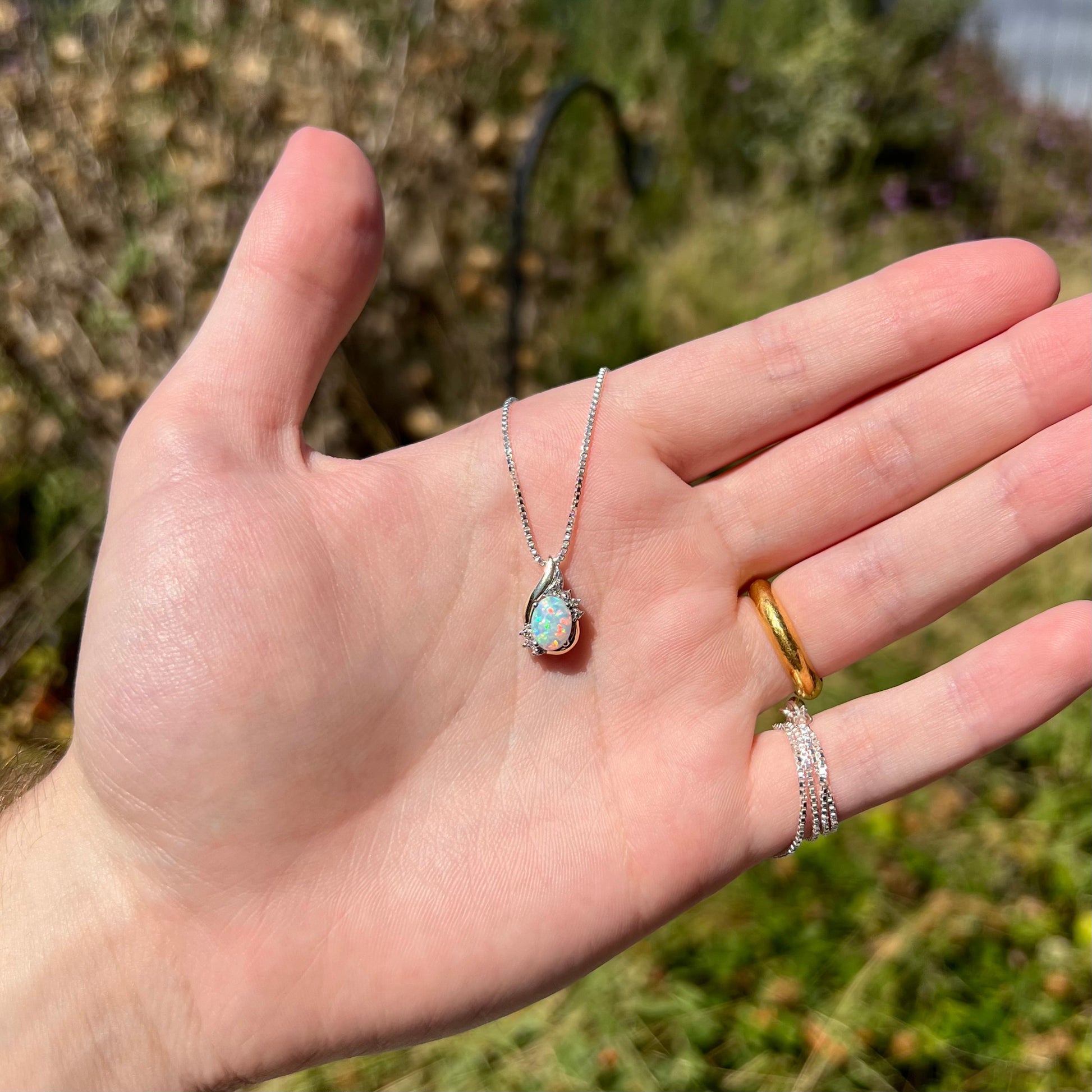 A dainty lab-created opal and diamond-accented necklace in two-tone sterling silver and 10k gold, held in a hand in sunlight.