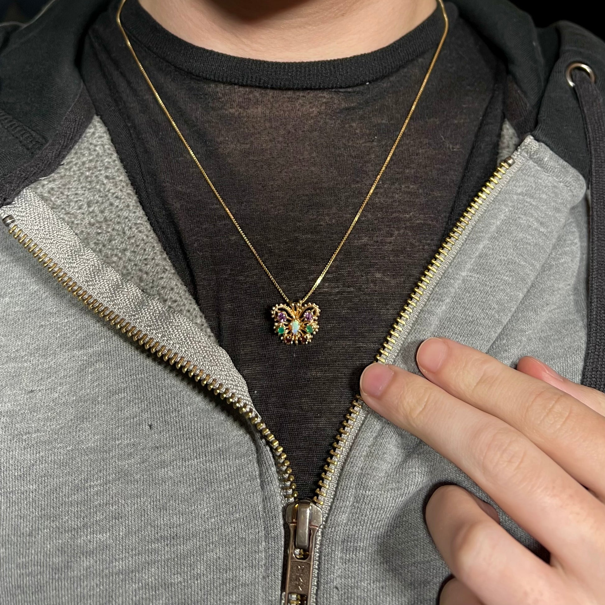 A dainty 14k gold ladies' opal and gemstone butterfly necklace worn around a person's neck against dark shirt.