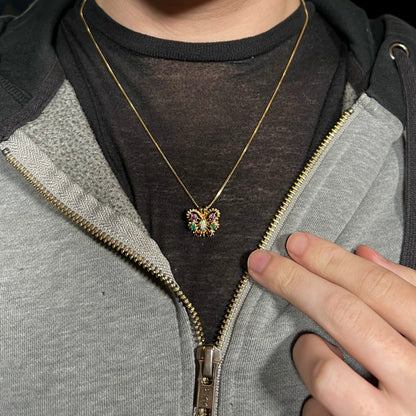 A dainty 14k gold ladies' opal and gemstone butterfly necklace worn around a person's neck against dark shirt.
