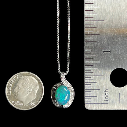 A dainty 1.72ct black opal and diamond pendant that measures two-thirds of an inch in length on chain between US dime coin and ruler for scale.