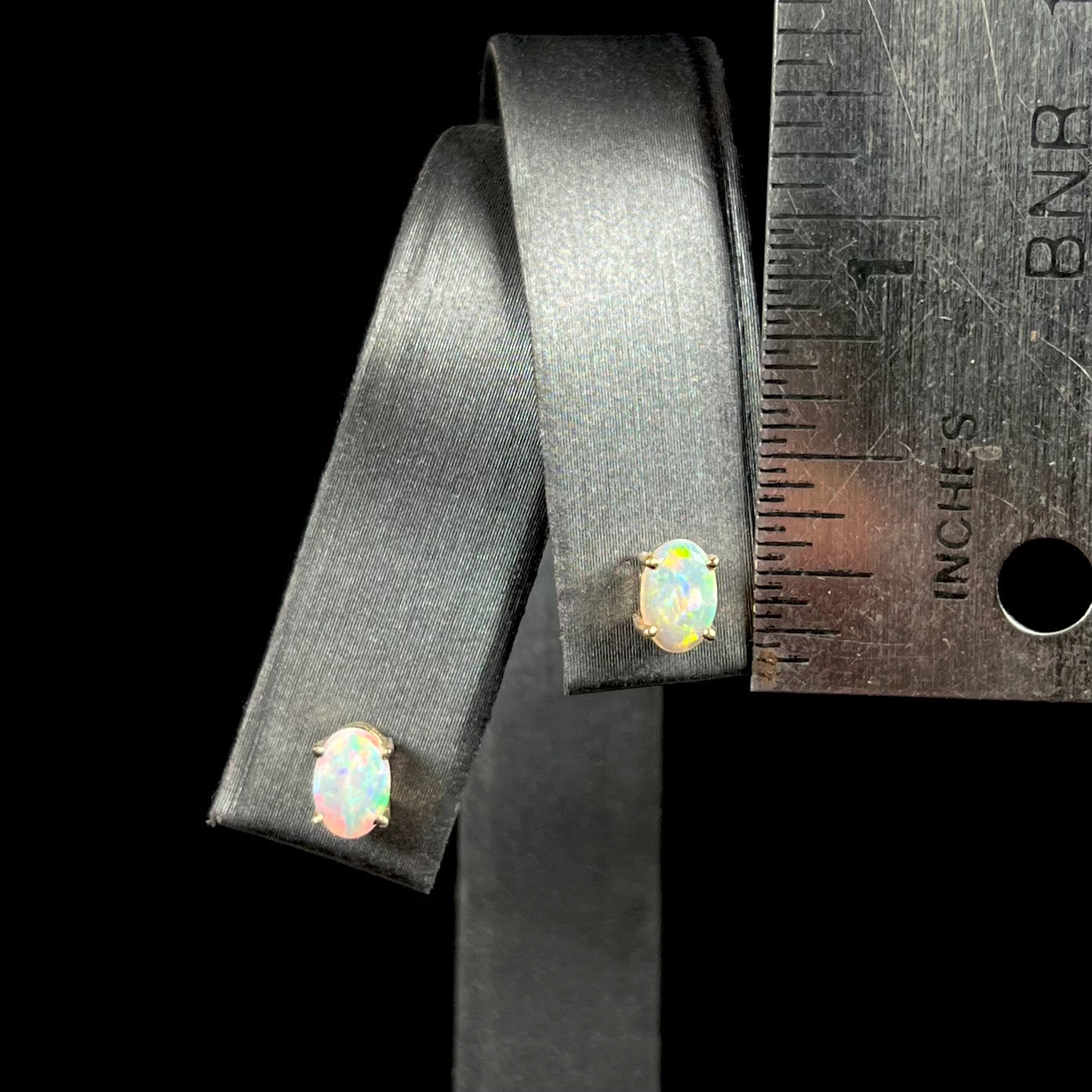 Dainty opal stud earrings next to a ruler for size comparison, measuring approximately 0.25 inches.