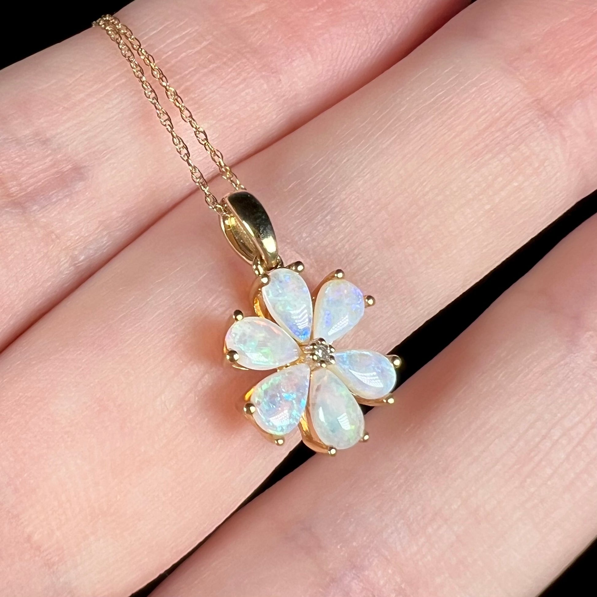 Dainty 10k gold pear shaped opal cluster necklace with flower design pendant shown close-up on fingers