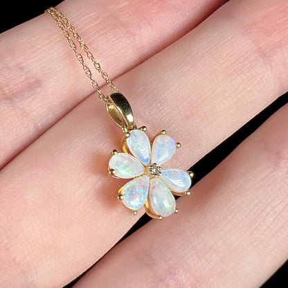 Dainty 10k gold pear shaped opal cluster necklace with flower design pendant shown close-up on fingers