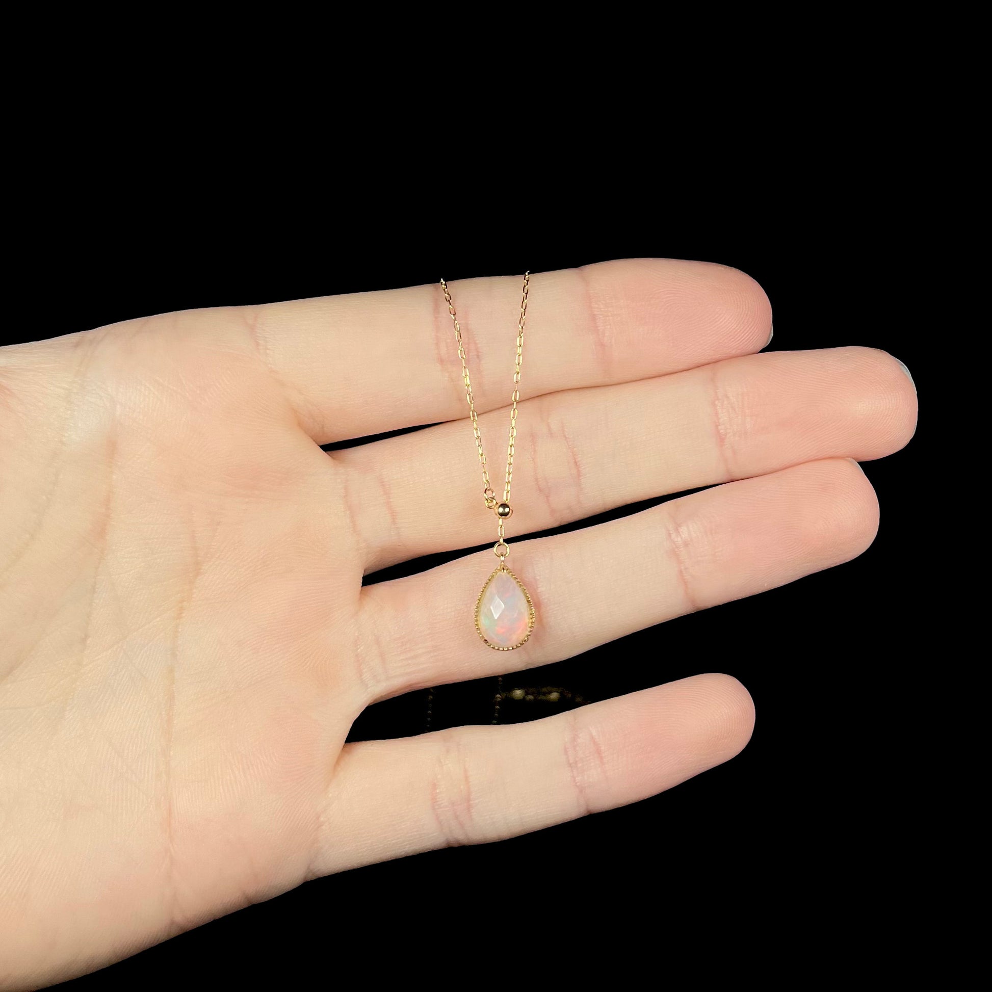 Dainty opal necklace resting on fingers, showing a very subtle red flash in the opal.