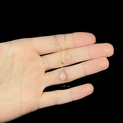 Dainty opal necklace resting on fingers, showing a very subtle red flash in the opal.