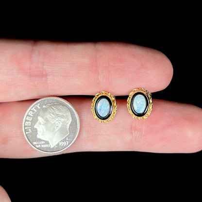 Dainty pair of opal and onyx stud earrings held between two fingers next to a US dime coin.