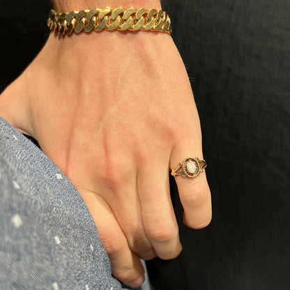 A ladies' Art Nouveau style opal solitaire ring.  The mounting is yellow gold with filigree accents.