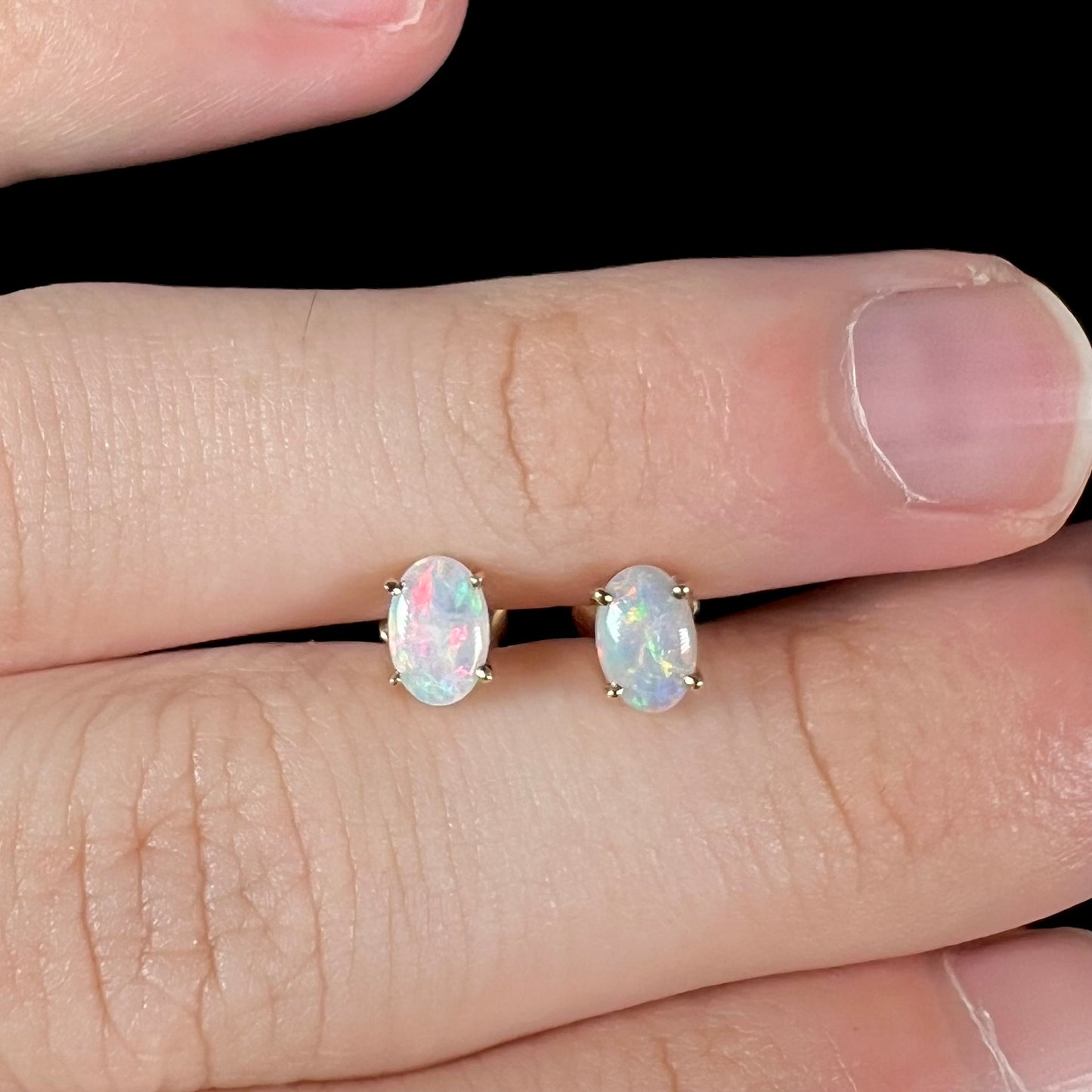 A macro close-up of dainty opal stud earrings, showing pink and green color play.