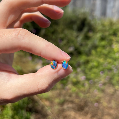 Pair of dainty opal triplet stud earrings in gold, held between two fingers in sunlight
