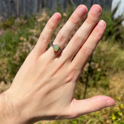 Hand wearing dainty women's sterling silver Ethiopian opal and blue apatite ring in sunlight