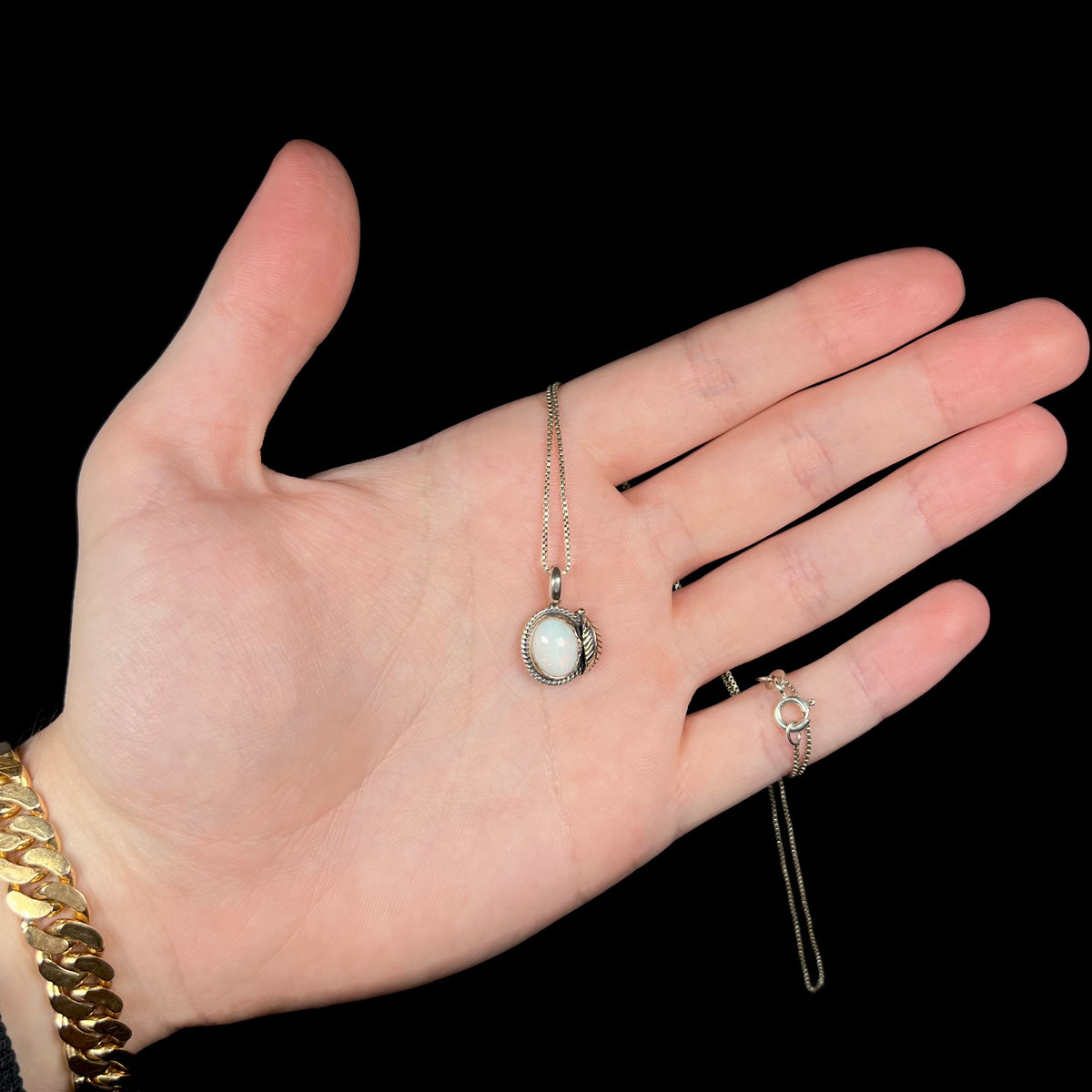 Hand holding dainty silver Australian opal pendant with American Southwest-inspired design