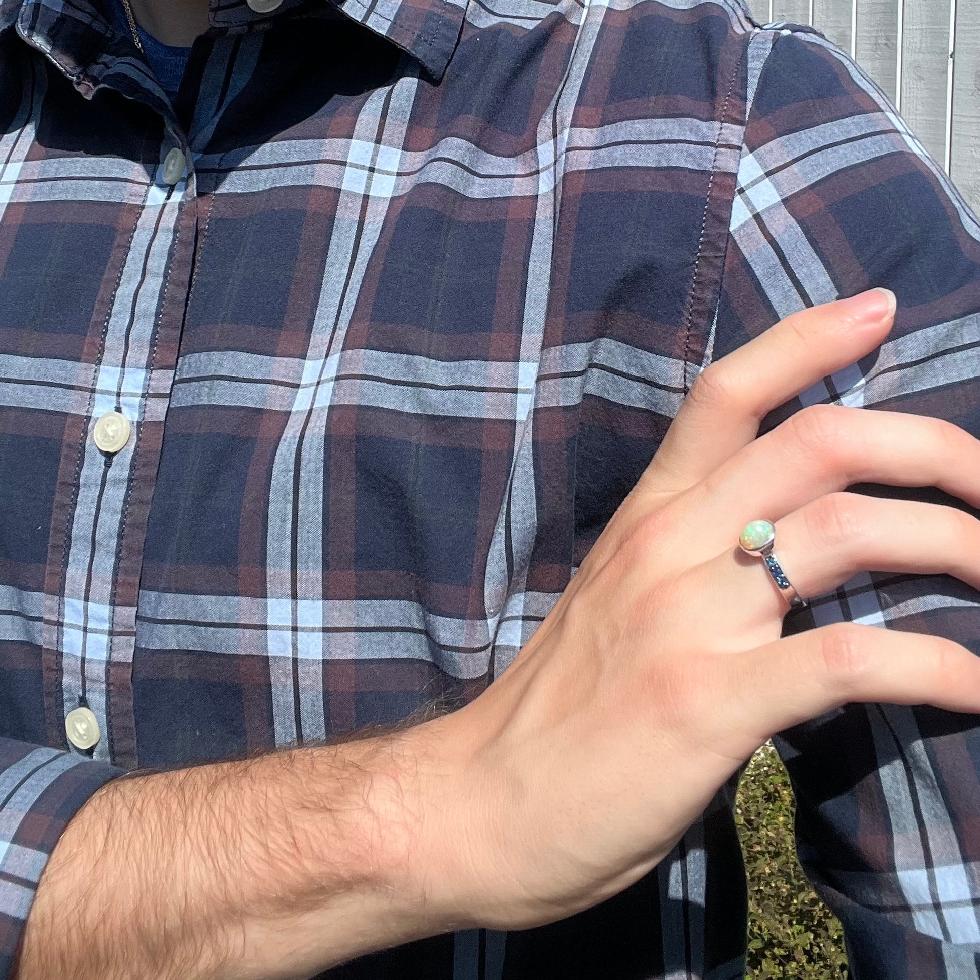 Person holding a hand on their shoulder, wearing a dainty silver opal ring in natural daylight.