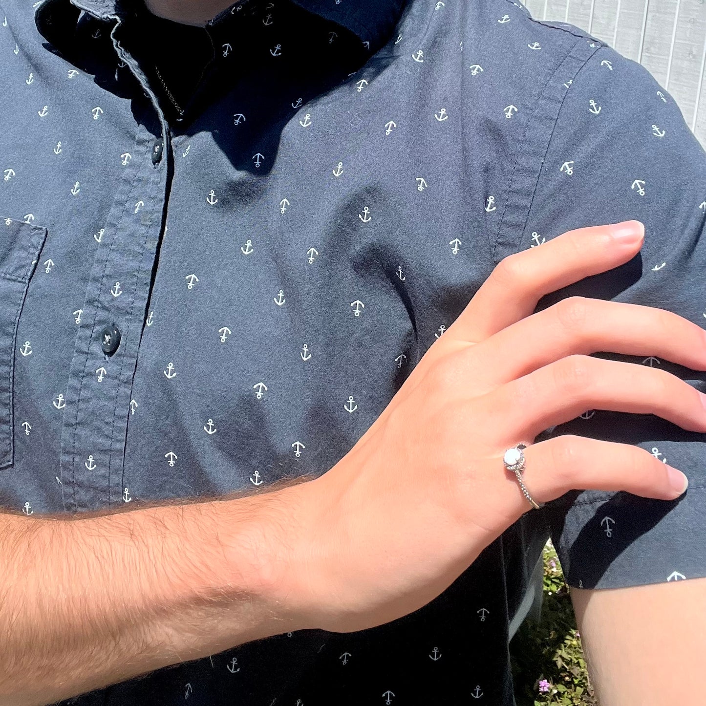 A dainty silver opal ring worn on the pinky finger of a hand as it rests on the model's opposing shoulder.