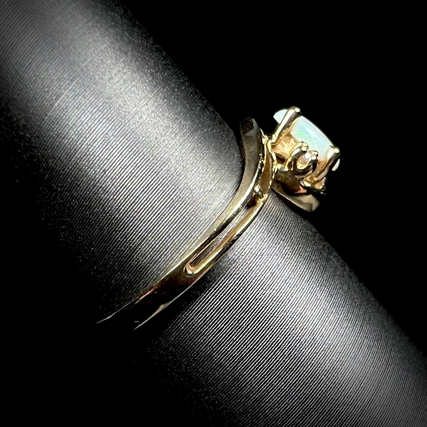 Side view of a dainty split shank opal ring in 10k yellow gold, shown on a ring display.