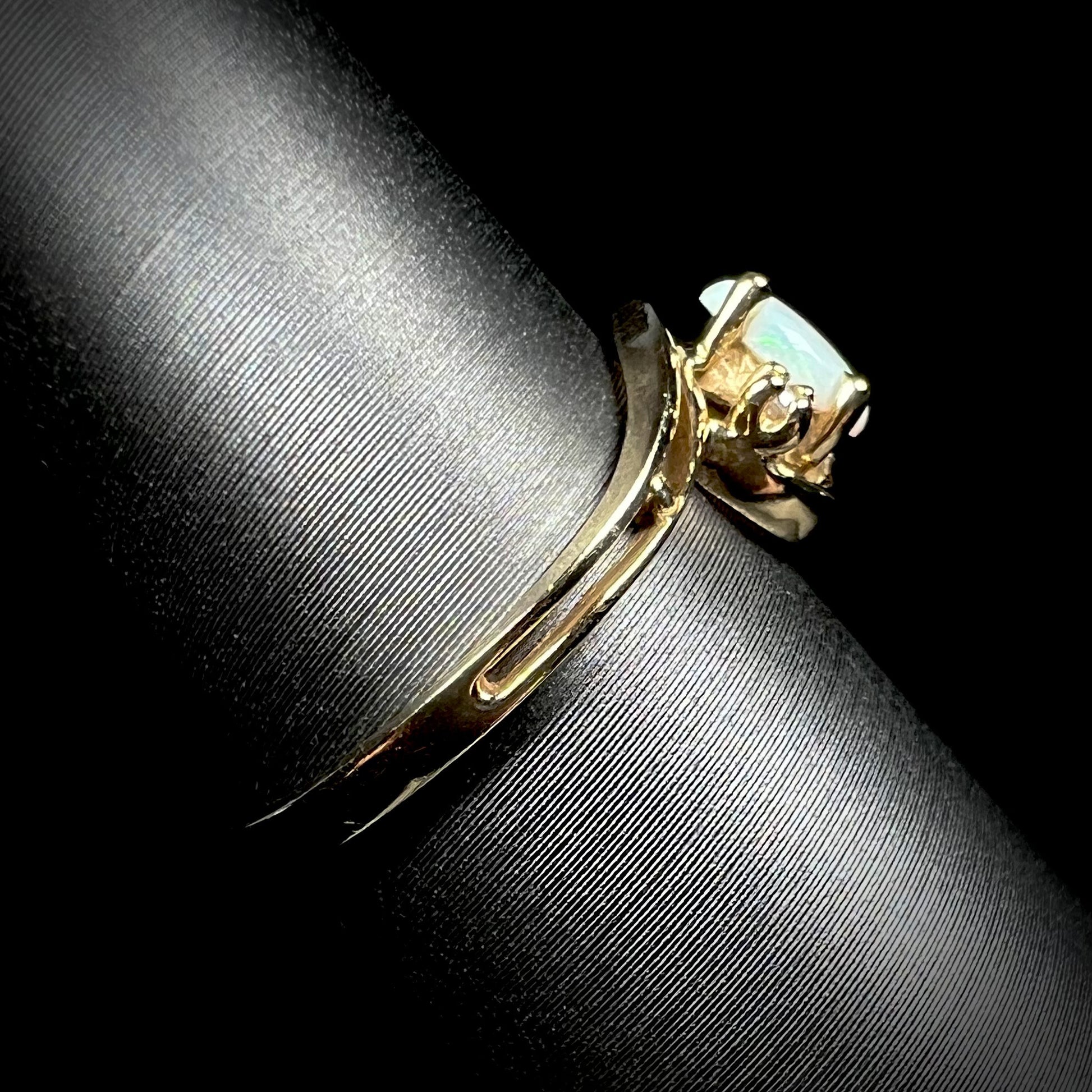Side view of a dainty split shank opal ring in 10k yellow gold, shown on a ring display.
