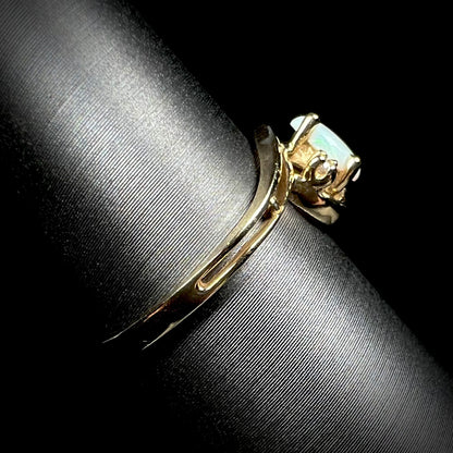 Side view of a dainty split shank opal ring in 10k yellow gold, shown on a ring display.