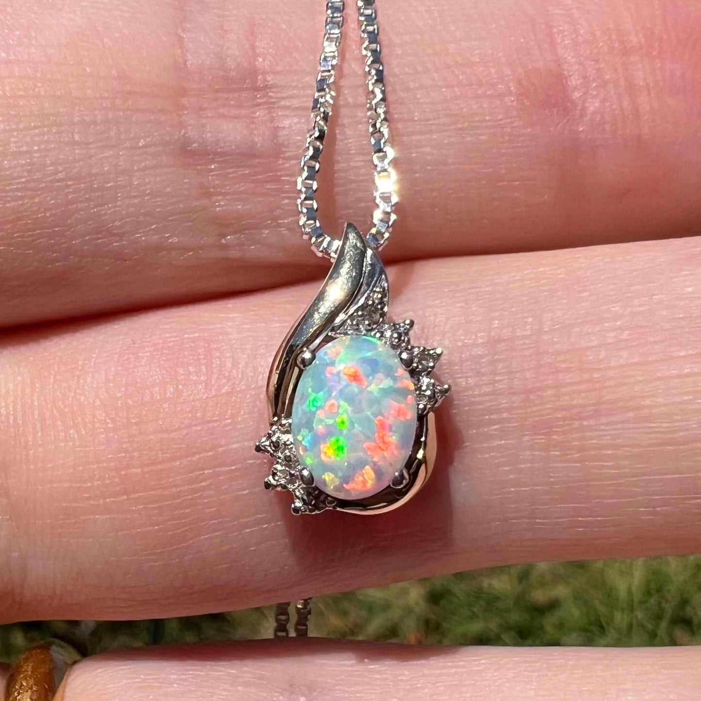 Close-up macro view of a dainty sterling silver and 10k gold opal and diamond pendant in natural light, resting on fingers.