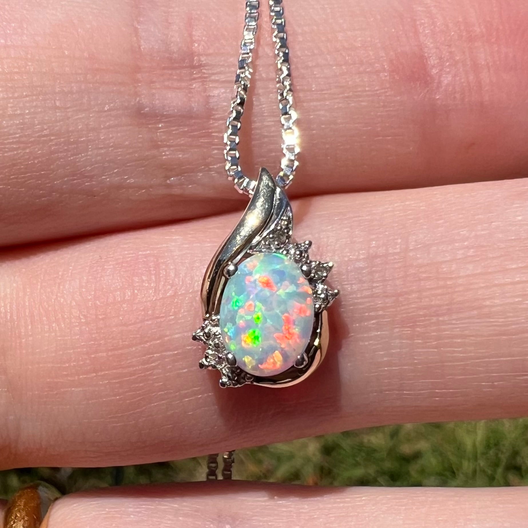 Close-up macro view of a dainty sterling silver and 10k gold opal and diamond pendant in natural light, resting on fingers.