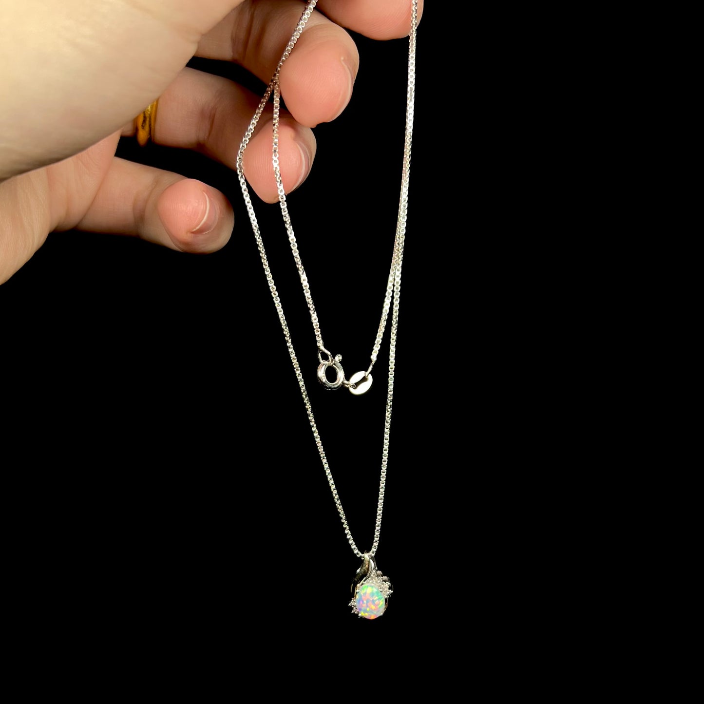 Hand dangling a dainty sterling silver lab-created opal and diamond necklace by its box-style silver chain.