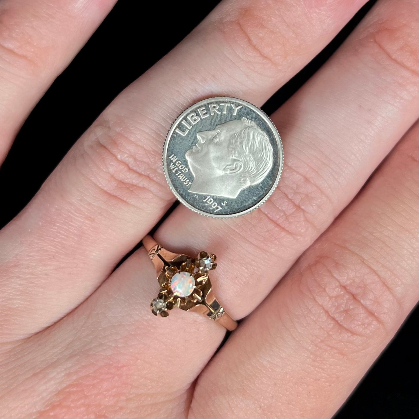 A dainty Victorian round opal and rose cut diamond ring worn on a hand.  A US dime coin sits on the hand next to the ring for scale.