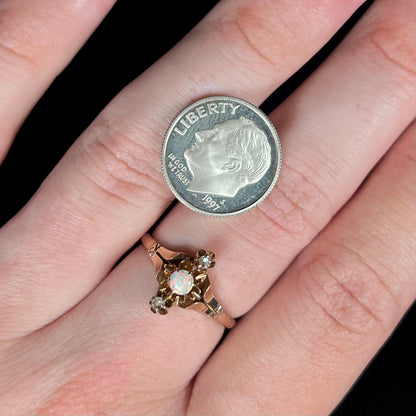 A dainty Victorian round opal and rose cut diamond ring worn on a hand.  A US dime coin sits on the hand next to the ring for scale.