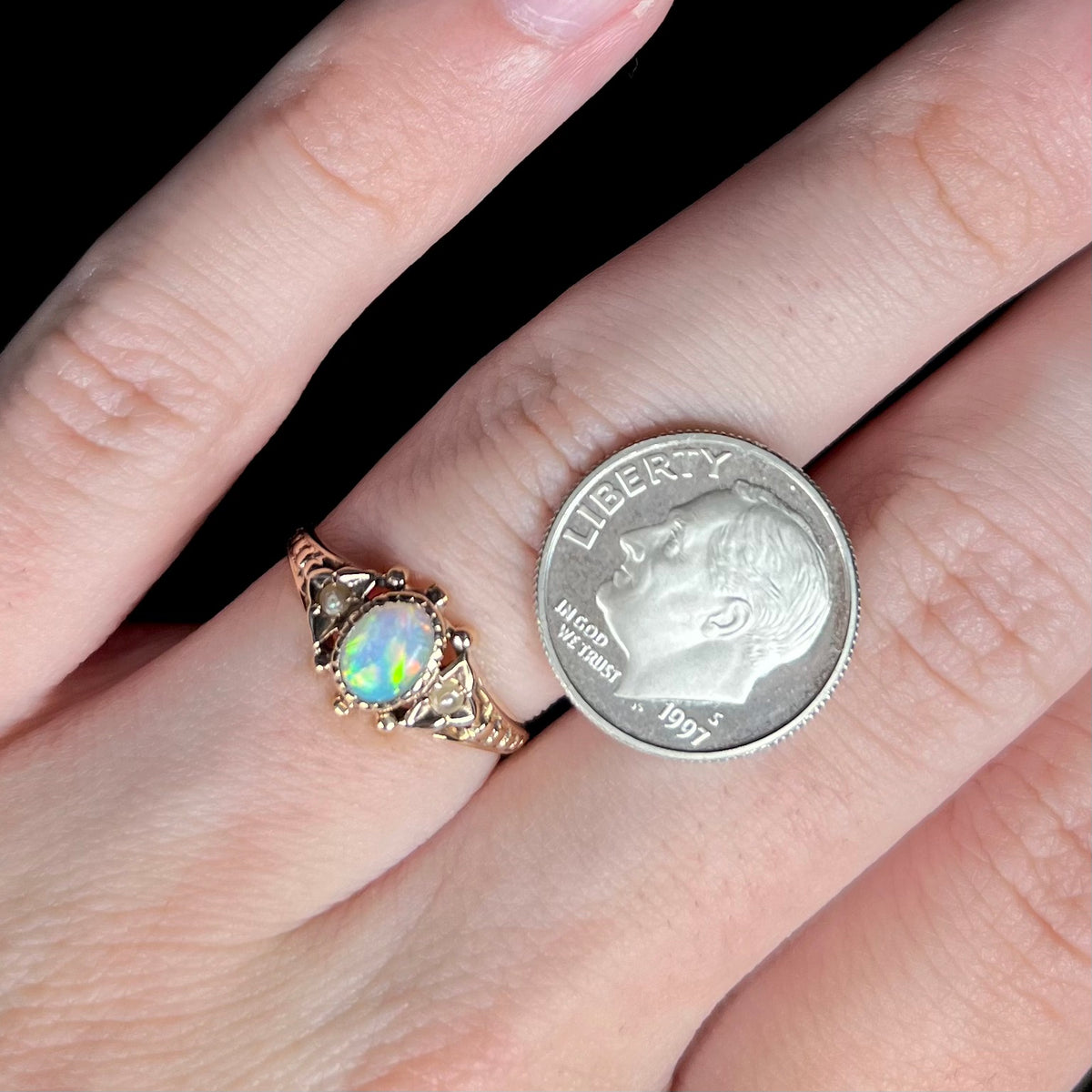 Close-up of hand wearing dainty Victorian opal and pearl ring in 9k gold next to US dime coin for scale