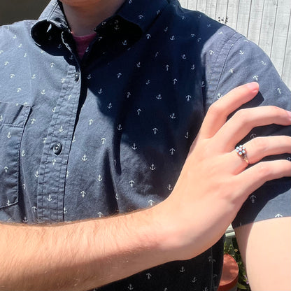 Close-up of person resting hand on opposing shoulder while wearing dainty Victorian opal and pink tourmaline ring