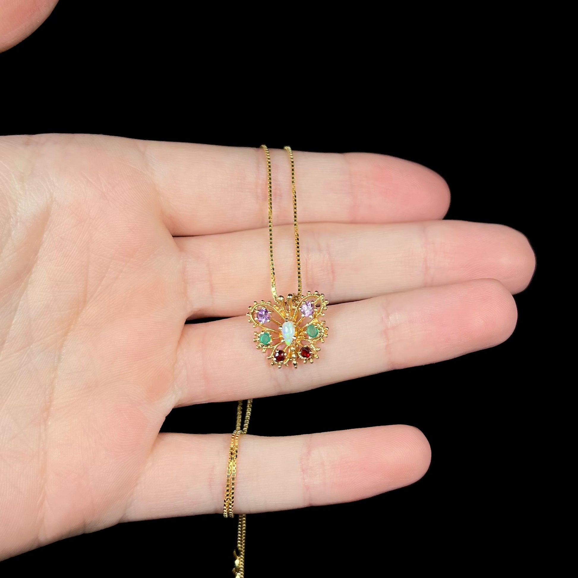 Hand holding a dainty, vintage, 1960s era gold butterfly necklace under LED studio light against black background.