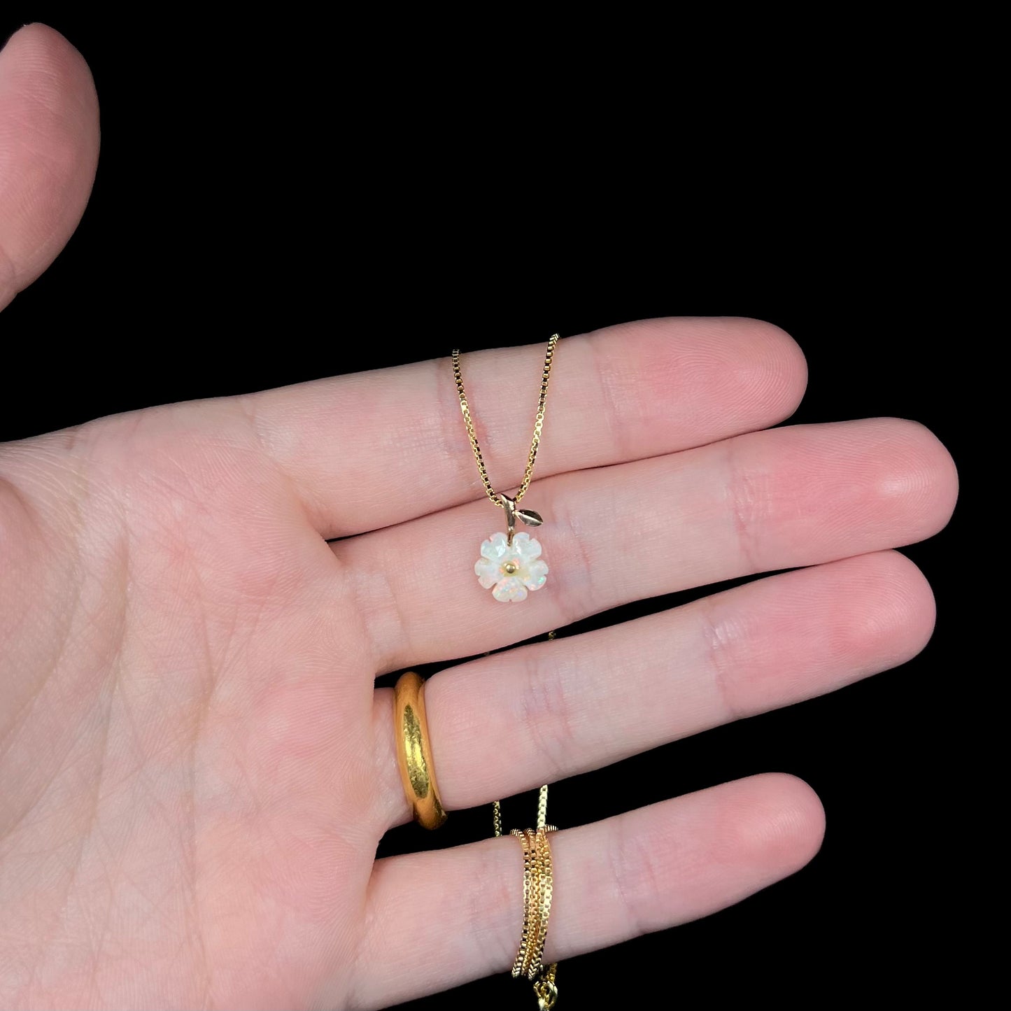 Hand holding a dainty carved white opal flower necklace in studio lighting against a black background.