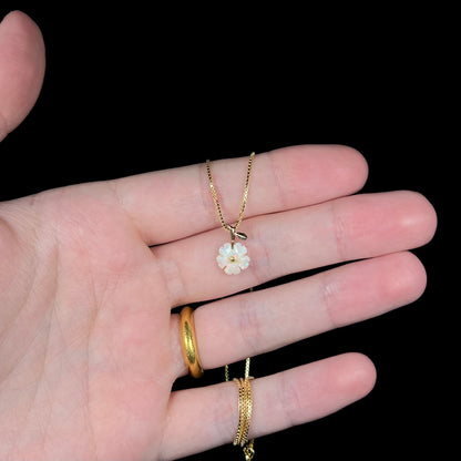 Hand holding a dainty carved white opal flower necklace in studio lighting against a black background.