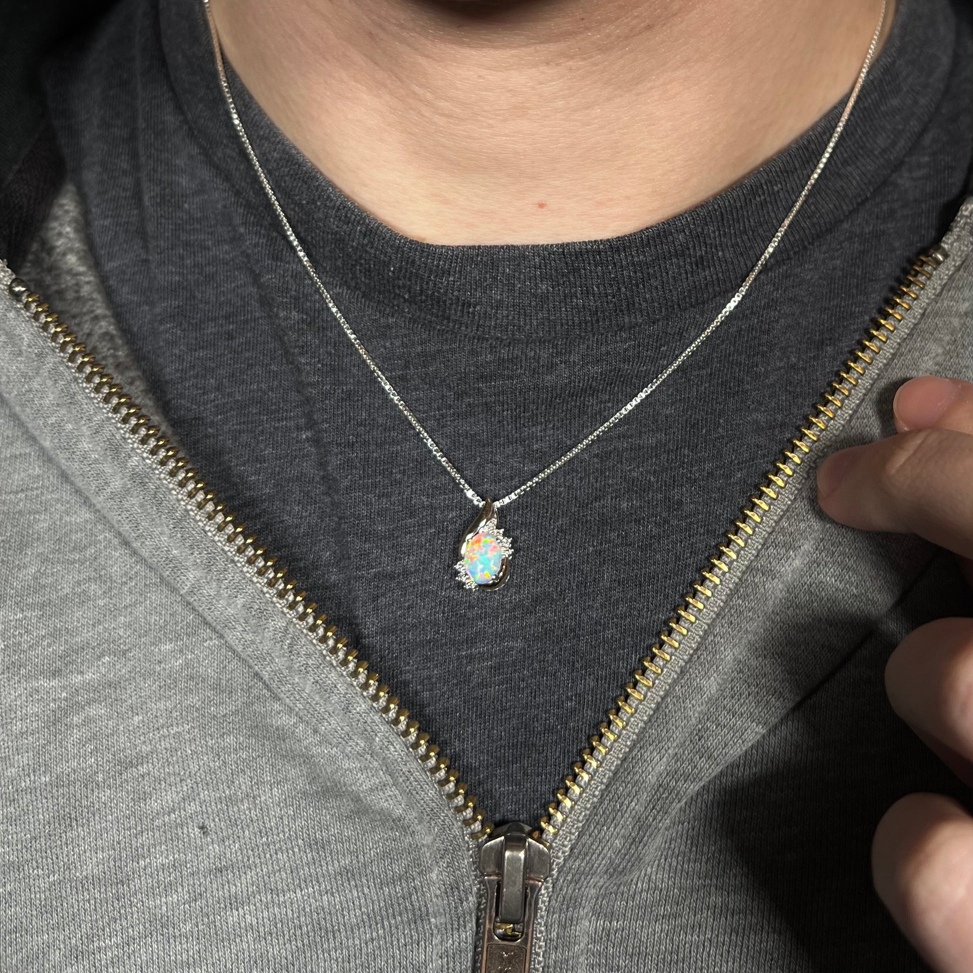 A dainty women's sterling silver opal and diamond necklace worn around a person's neck against dark shirt beneath hoodie.