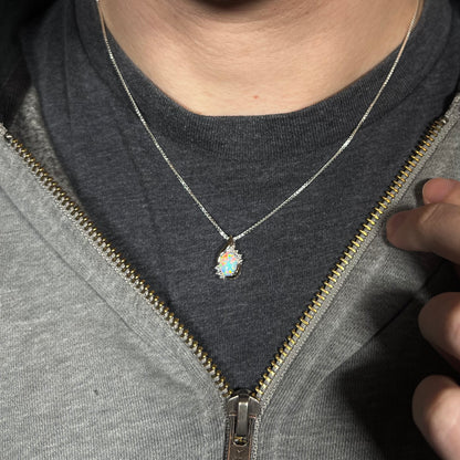 A dainty women's sterling silver opal and diamond necklace worn around a person's neck against dark shirt beneath hoodie.