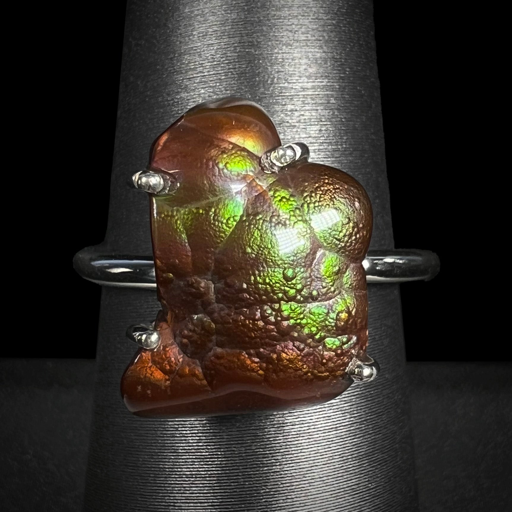 Macro shot of a Deer Creek fire agate ring on a gray ring holder with green iridescence visible.