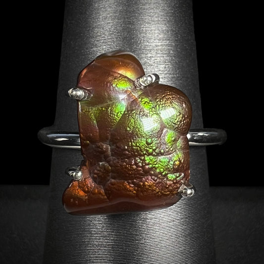 Macro shot of a Deer Creek fire agate ring on a gray ring holder with green iridescence visible.
