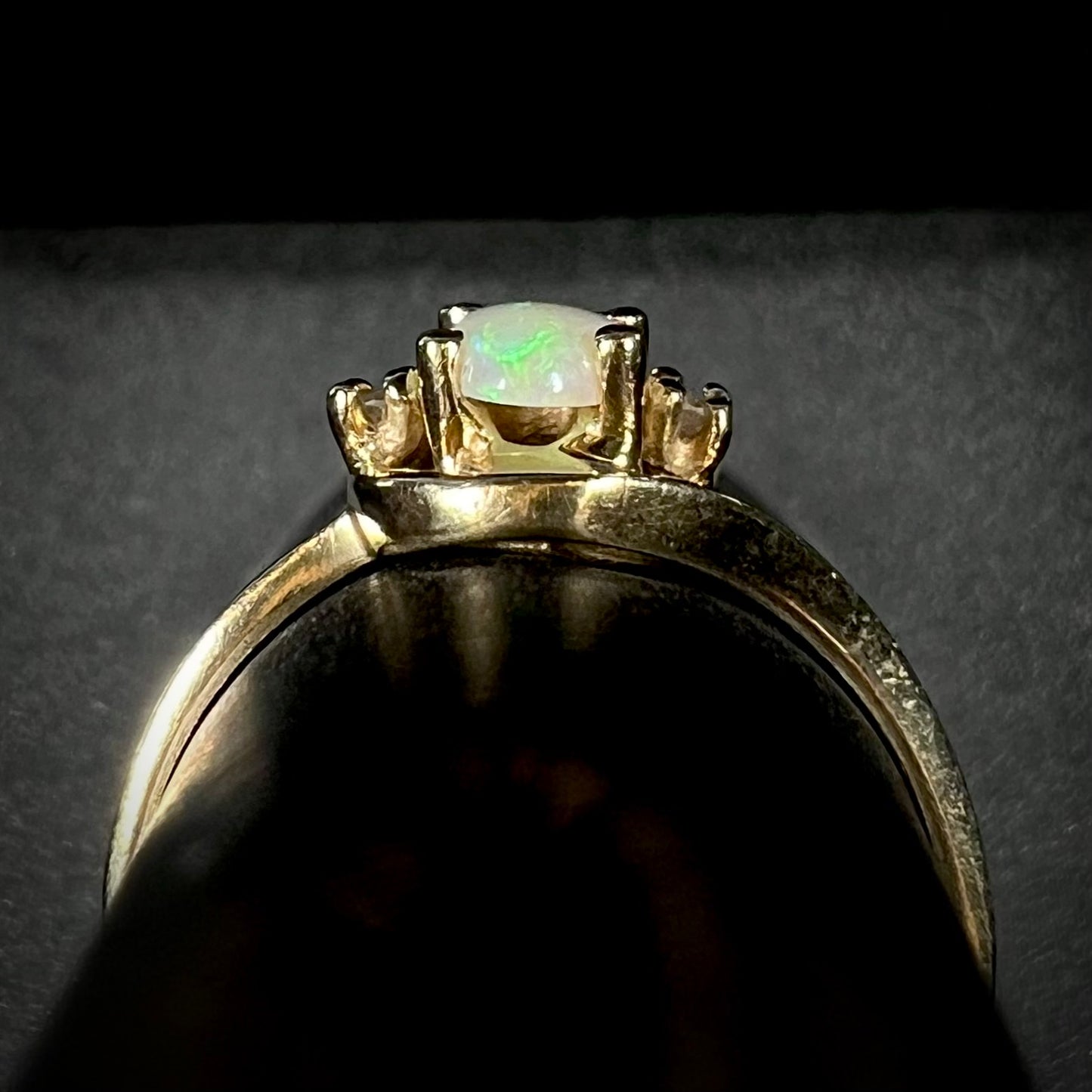 Side gallery view of a delicate 10k yellow gold opal and diamond ring on a ring display.