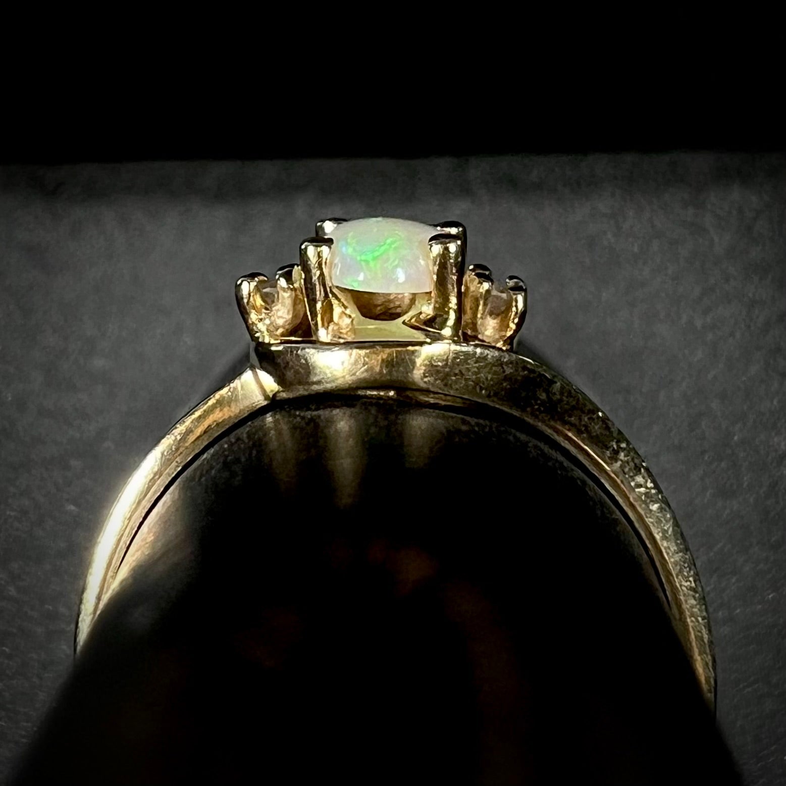 Side gallery view of a delicate 10k yellow gold opal and diamond ring on a ring display.
