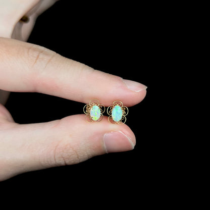 Pair of delicate 14k gold opal stud earrings with filigree flower design, held between two fingers