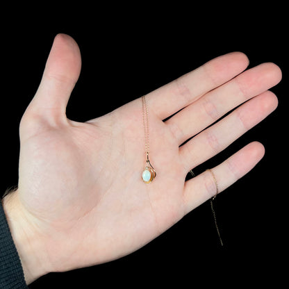Hand holding a delicate gold Australian opal and diamond necklace, the pendant's chain wrapped around the hand's pinky finger