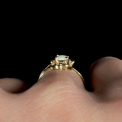 Side gallery view of a delicate gold opal ring, worn on a hand.