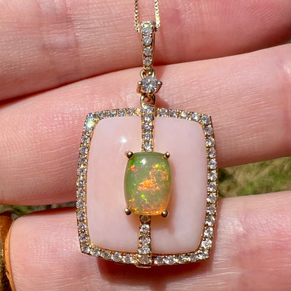 Macro close-up of a women's 14k gold Ethiopian opal and diamond pave halo pendant by designer, Cirari, held in a hand in sunlight.