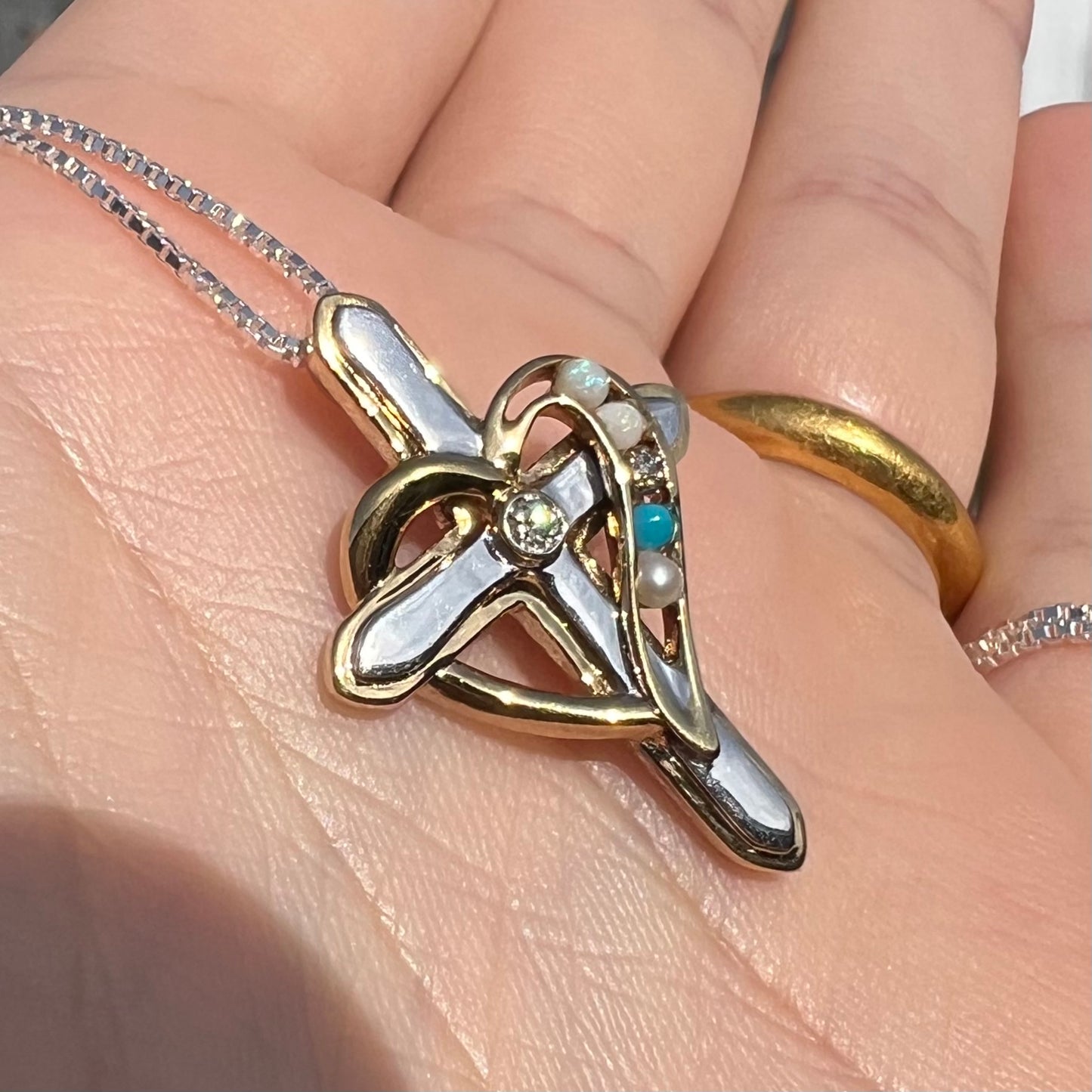 A two-tone sterling silver mother's cross necklace set with diamond, opal, turquoise, and pearl, shown in sunlight.