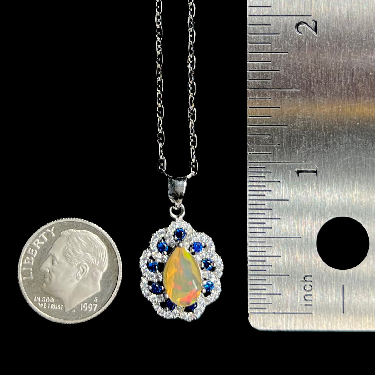 Women's silver Ethiopian opal and blue sapphire necklace shown next to US dime coin and ruler; the pendant is similar in size to the dime