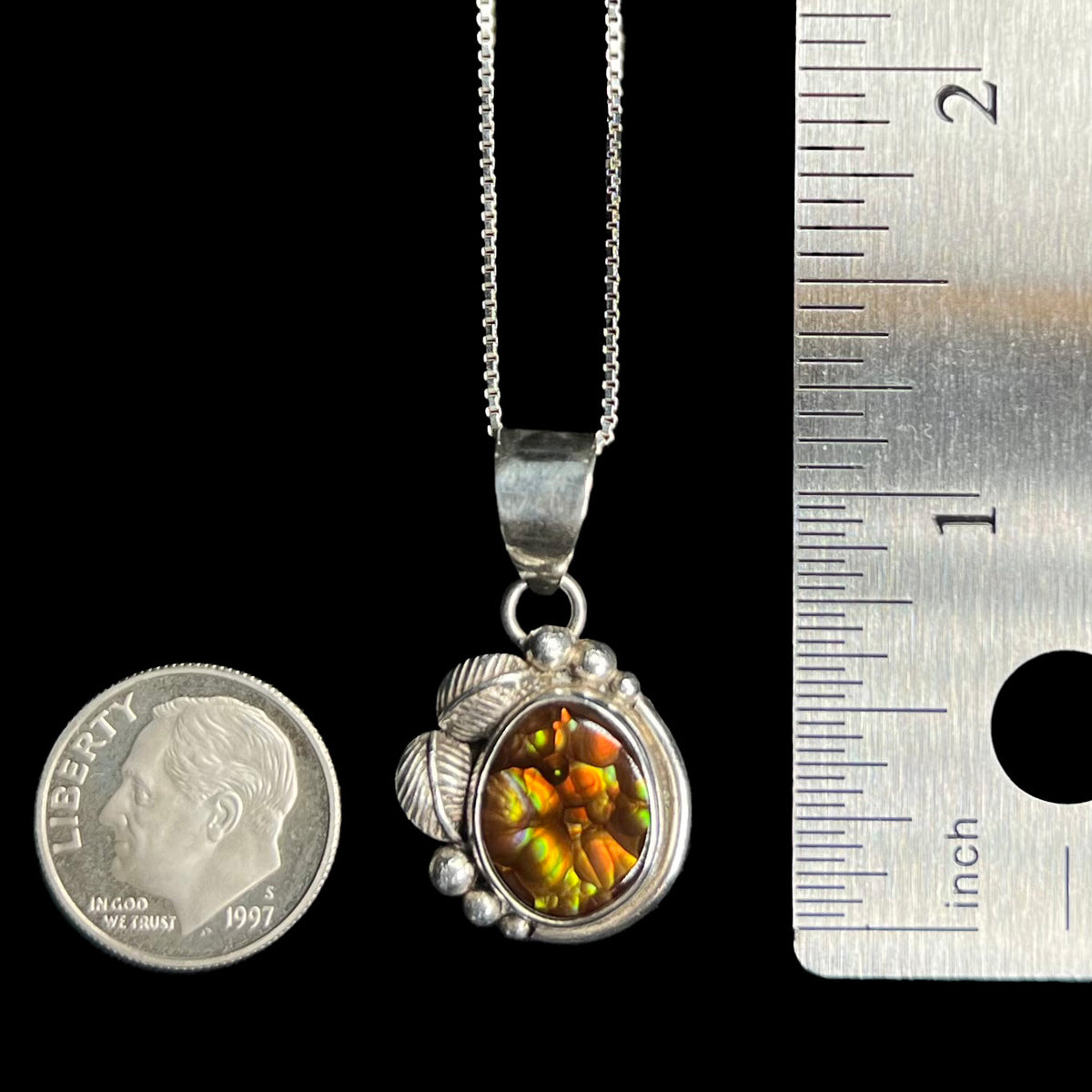 A silver fire agate pendant measuring 1.2 inches long from top of bail shown on chain between US dime coin and ruler.  Excluding the bail, the pendant is roughly the size of the dime.