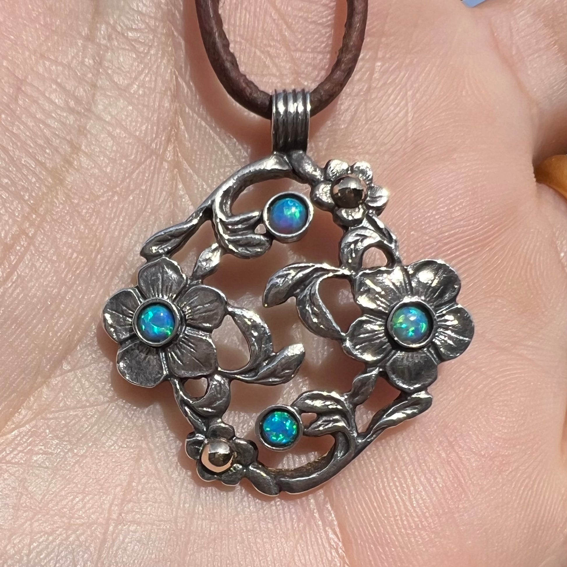 A two-tone sterling silver and 14k gold opal dogwood flower pendant shown close-up in a hand in sunlight.