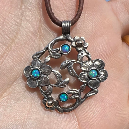 A two-tone sterling silver and 14k gold opal dogwood flower pendant shown close-up in a hand in sunlight.