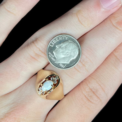 Close-up of hand wearing a domed Mid-Century style opal and diamond ring in 14k gold next to a US dime coin for scale