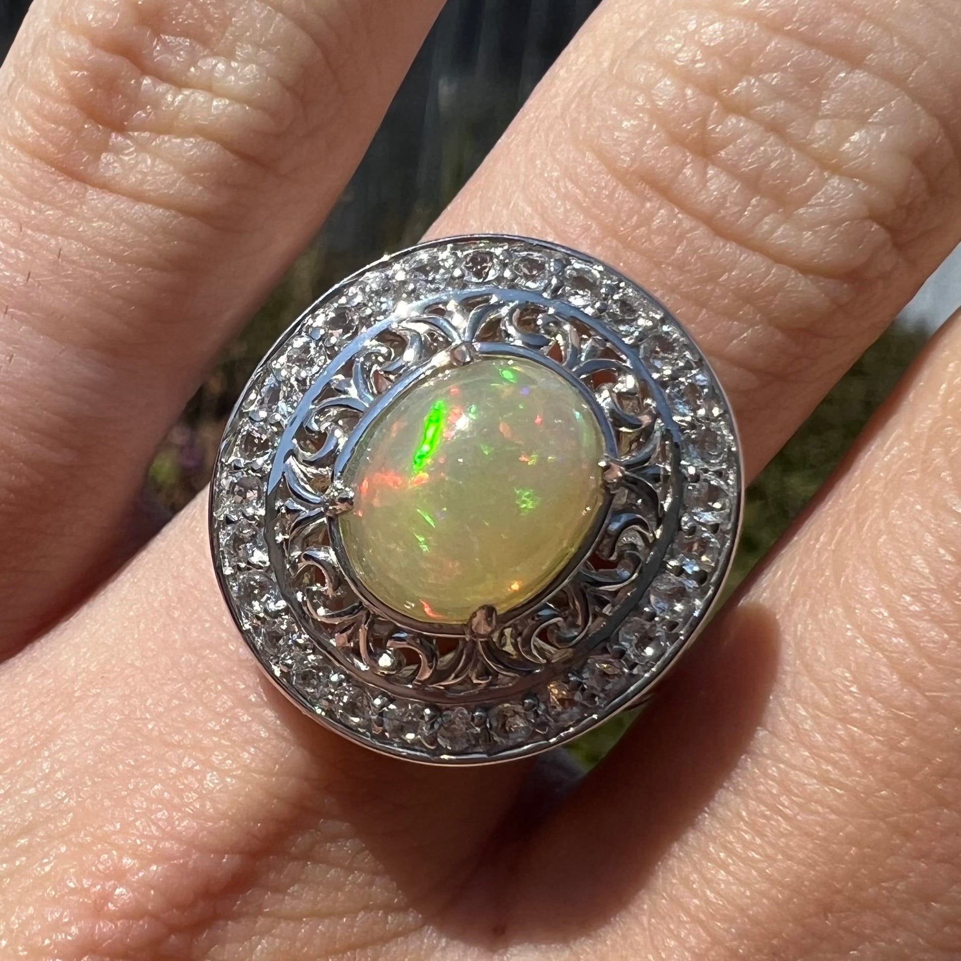 Close-up of finger wearing a double halo opal ring in natural sunlight.
